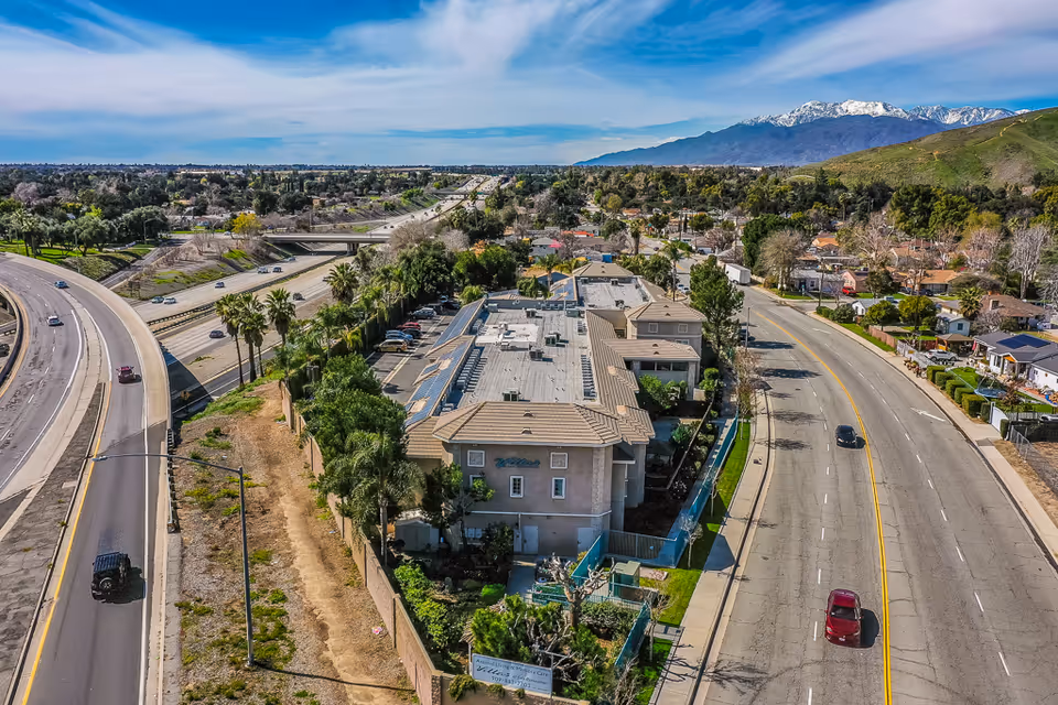 Aerial view of a multi-building residential complex next to a highway and a city street with mountains in the distance.