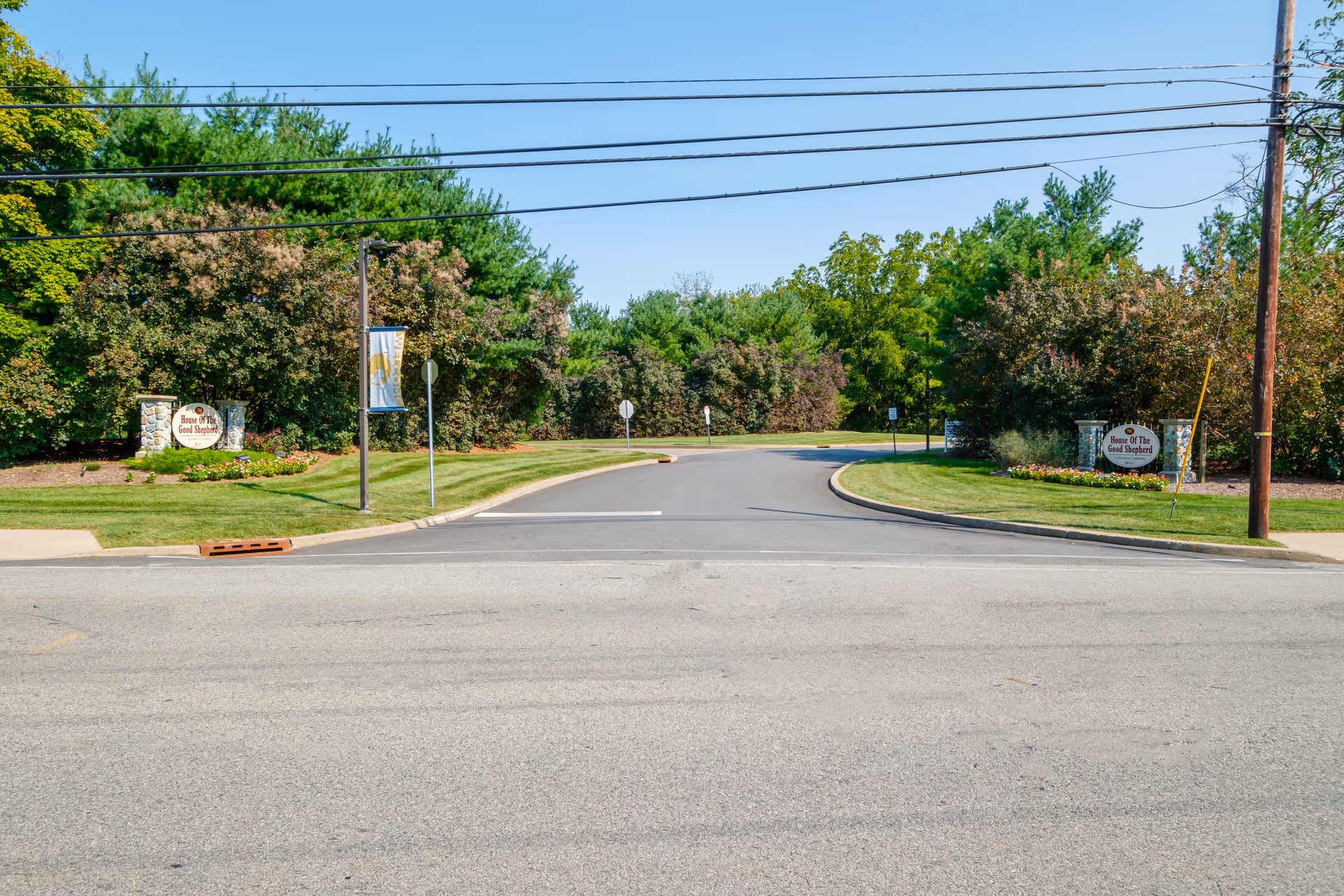 Entrance roadway to Riverwalk Village at The House of The Good Shepherd flanked by landscaped lawns and stone signs.