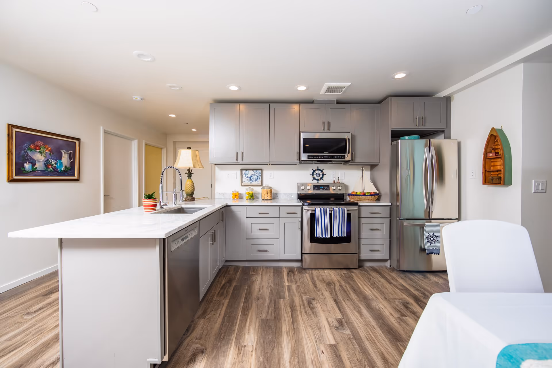 Bright modern kitchen with gray cabinets, stainless steel appliances, a marble island, and wood-look flooring.