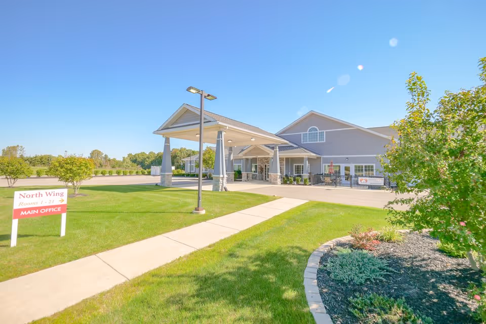 Front entrance of a single-story senior living facility with a covered porte-cochere, sidewalk, lawn, and a North Wing sign.