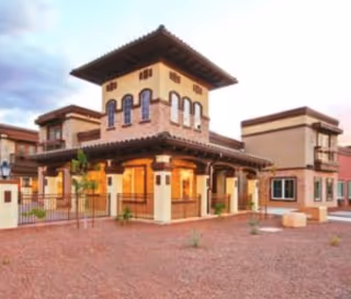 Mediterranean-style senior living building with a central tower, covered entrance, and surrounding courtyard.