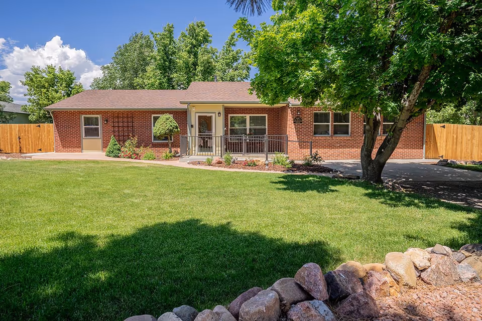 Brick, single-story assisted living building with manicured lawn and shaded front entrance.