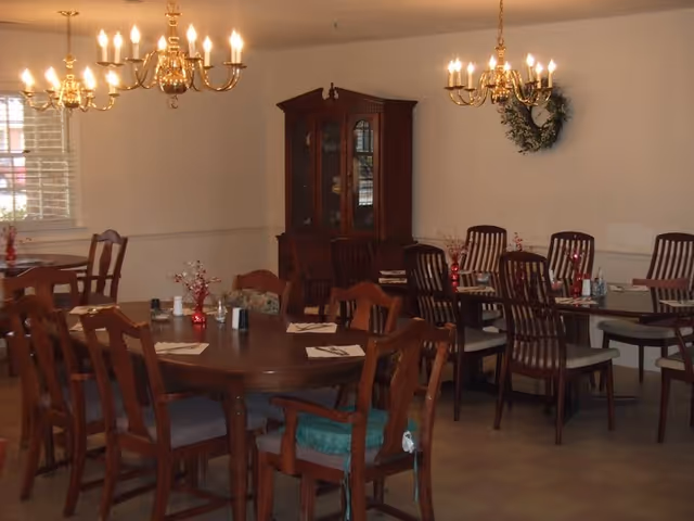 A dining room with several wooden tables and chairs, brass chandeliers, place settings, and a china cabinet against the wall.