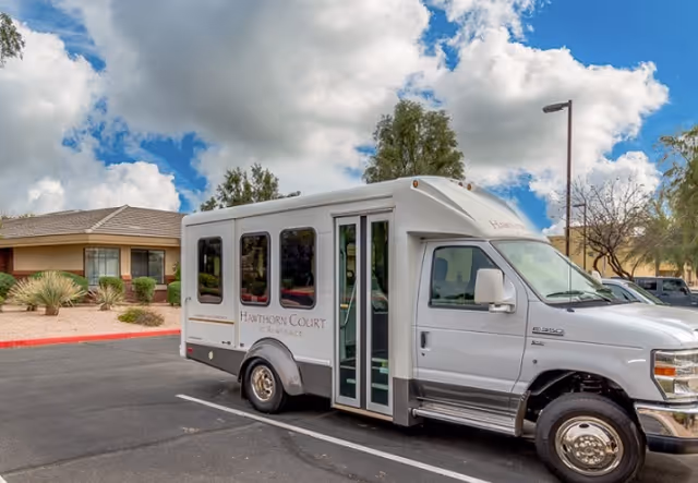 White shuttle bus parked in a lot outside a memory care facility on a sunny day.