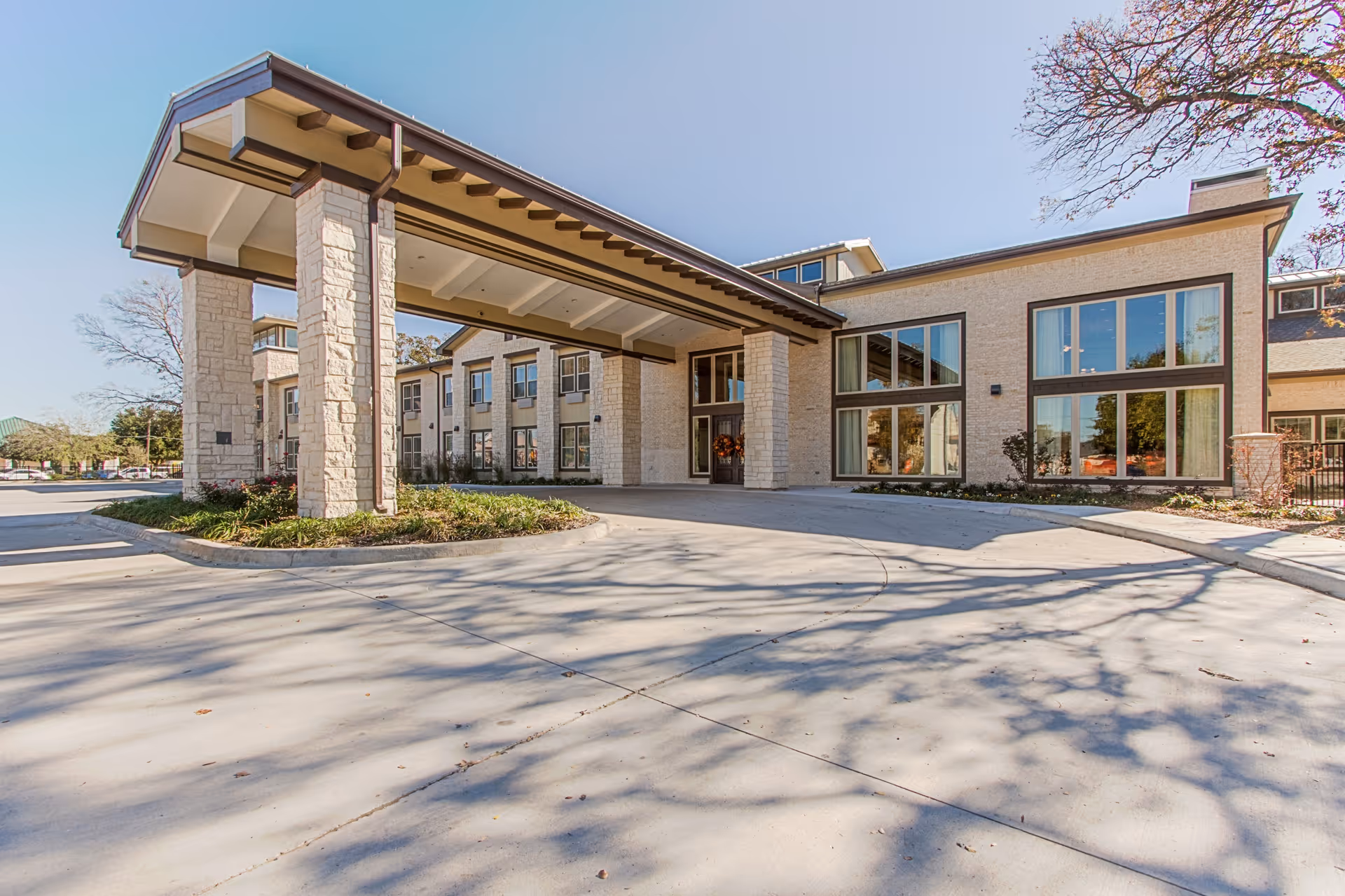 Front entrance of a senior living building with a covered porte-cochere, large windows, and a paved driveway.