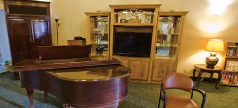 A spacious living room-style lounge with a grand piano and an entertainment cabinet.