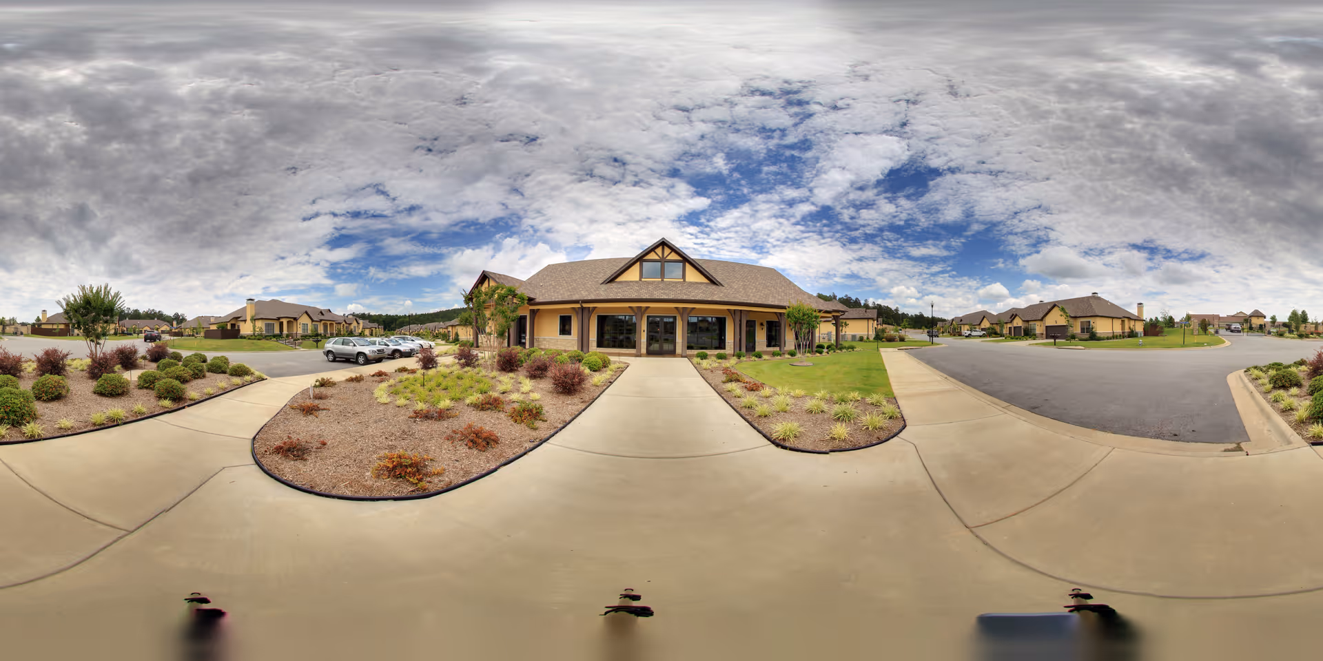 Front exterior of the Villas of Chenal single-story building with a covered entrance, landscaped drive, and cloudy sky.