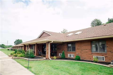 Exterior view of a single-story brick building with a sloped roof and skylights, surrounded by a well-maintained lawn and some shrubs under a partly cloudy sky.