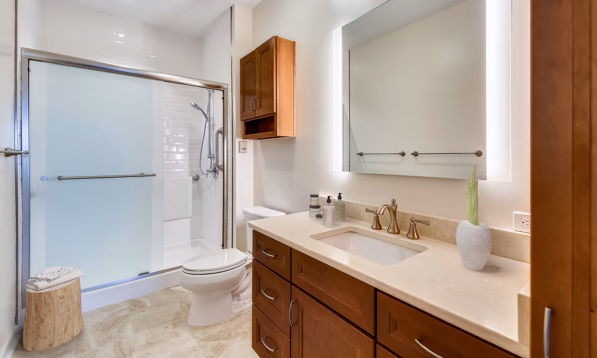 Bright modern bathroom with a frosted glass sliding shower, toilet, and wood vanity with illuminated mirror.