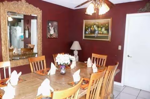 Wooden dining table with folded napkins, chairs, and burgundy dining room walls.