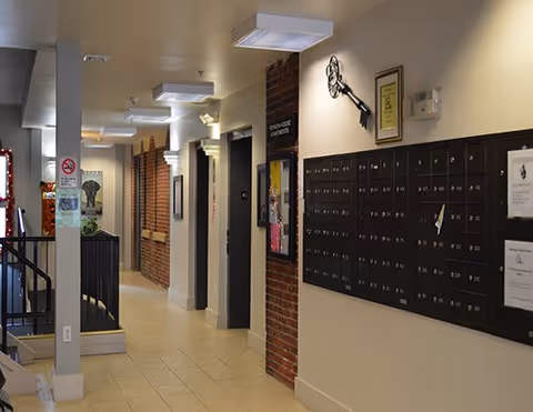 Interior hallway of Vernon House facility with a row of mailboxes mounted on the right wall, brick accents, and doors leading to other rooms. The hallway is well-lit with ceiling lights and has tiled flooring.