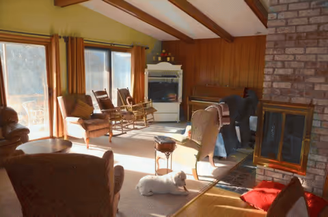 Cozy living room featuring wooden beams, a brick fireplace, and a small white dog.