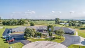 Aerial view of a single-story senior living facility named Wayside Parkview Estates surrounded by green lawns and trees, with a circular driveway and several parked cars. The background shows open fields and a partly cloudy sky.