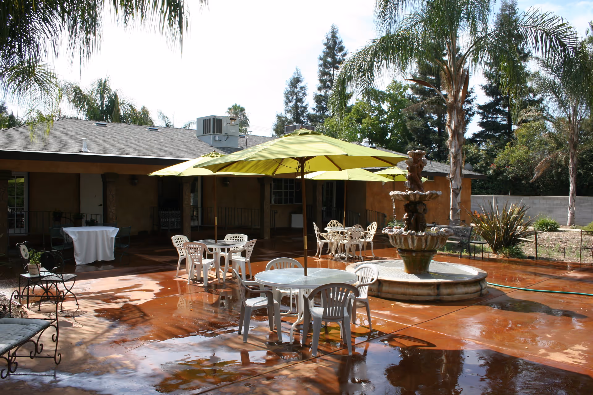 Outdoor courtyard patio with green umbrellas, plastic tables and chairs surrounding a central fountain.