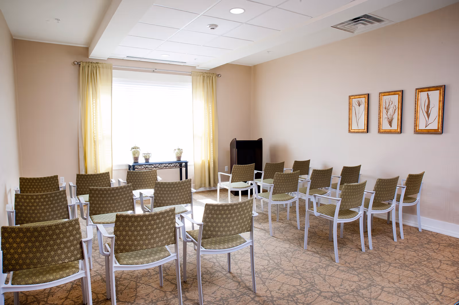 Bright meeting room with rows of green patterned chairs facing a window and a small podium.