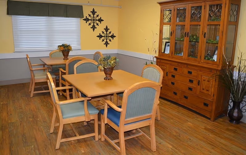 Small dining room with wooden tables and upholstered chairs, a wooden hutch, and wall decorations.