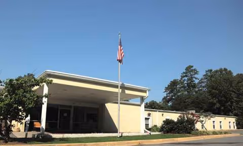 Single-story nursing center exterior with flagpole and blue sky in front.