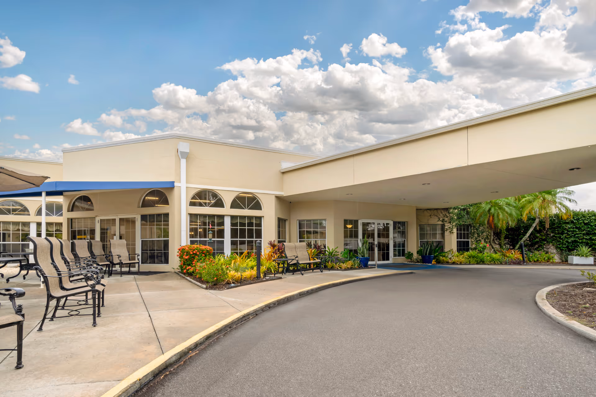 Exterior view of Aspire at Bradenton's entrance, featuring a covered walkway, seating area, and landscaped gardens.