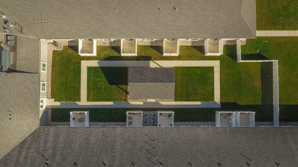 Aerial view of a rectangular interior courtyard with walkways, green lawns, small fenced patios and surrounding building roofs.