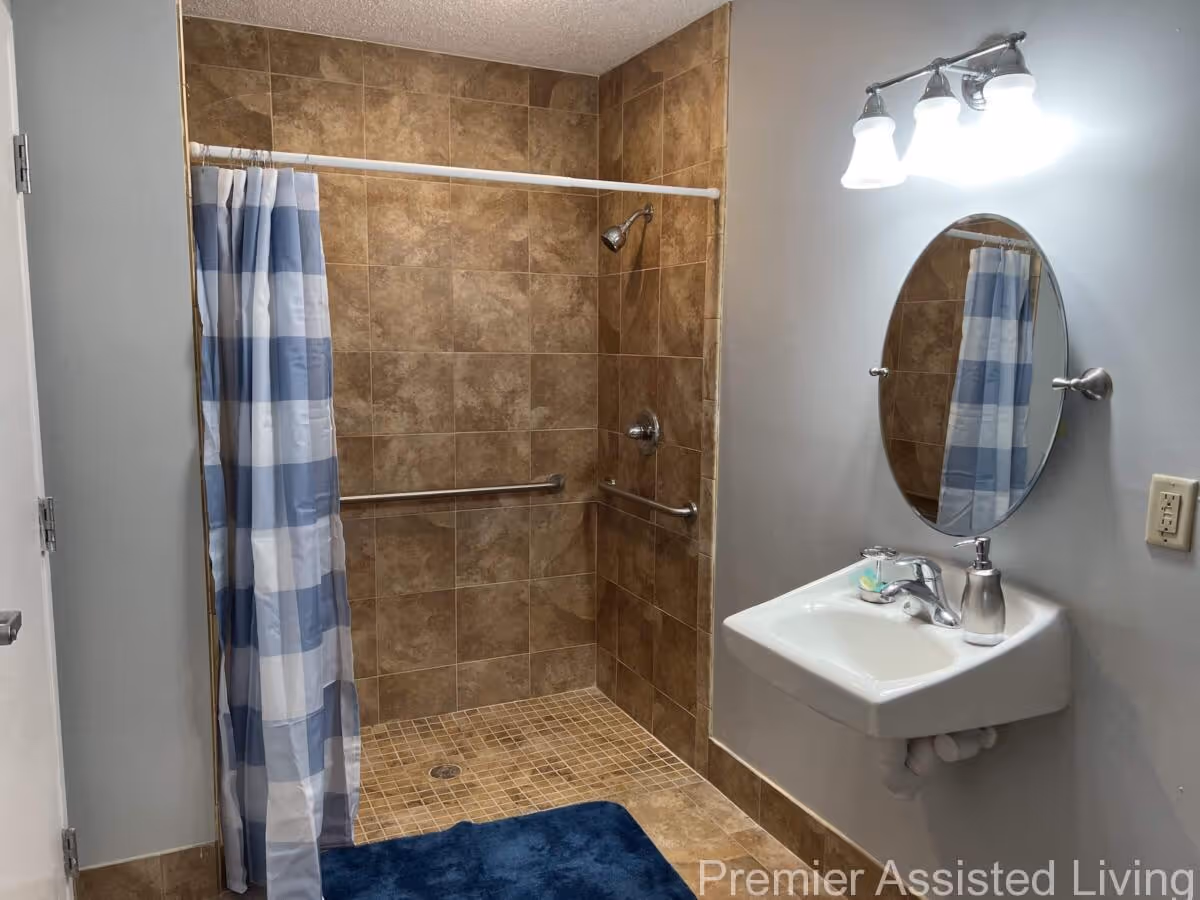 Accessible bathroom with a tiled walk-in shower with grab bars, a blue checkered shower curtain, wall-mounted sink and oval mirror.