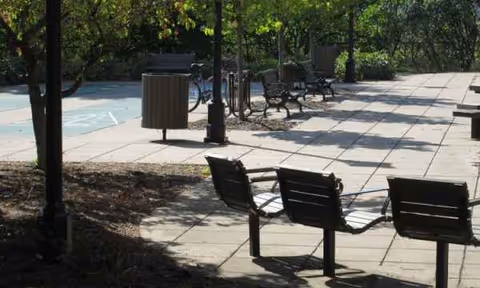 Outdoor courtyard with benches, trash can, trees, and paved seating area.