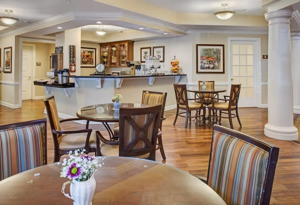 Bright common dining area with round tables, striped chairs, a coffee bar and decorative columns.