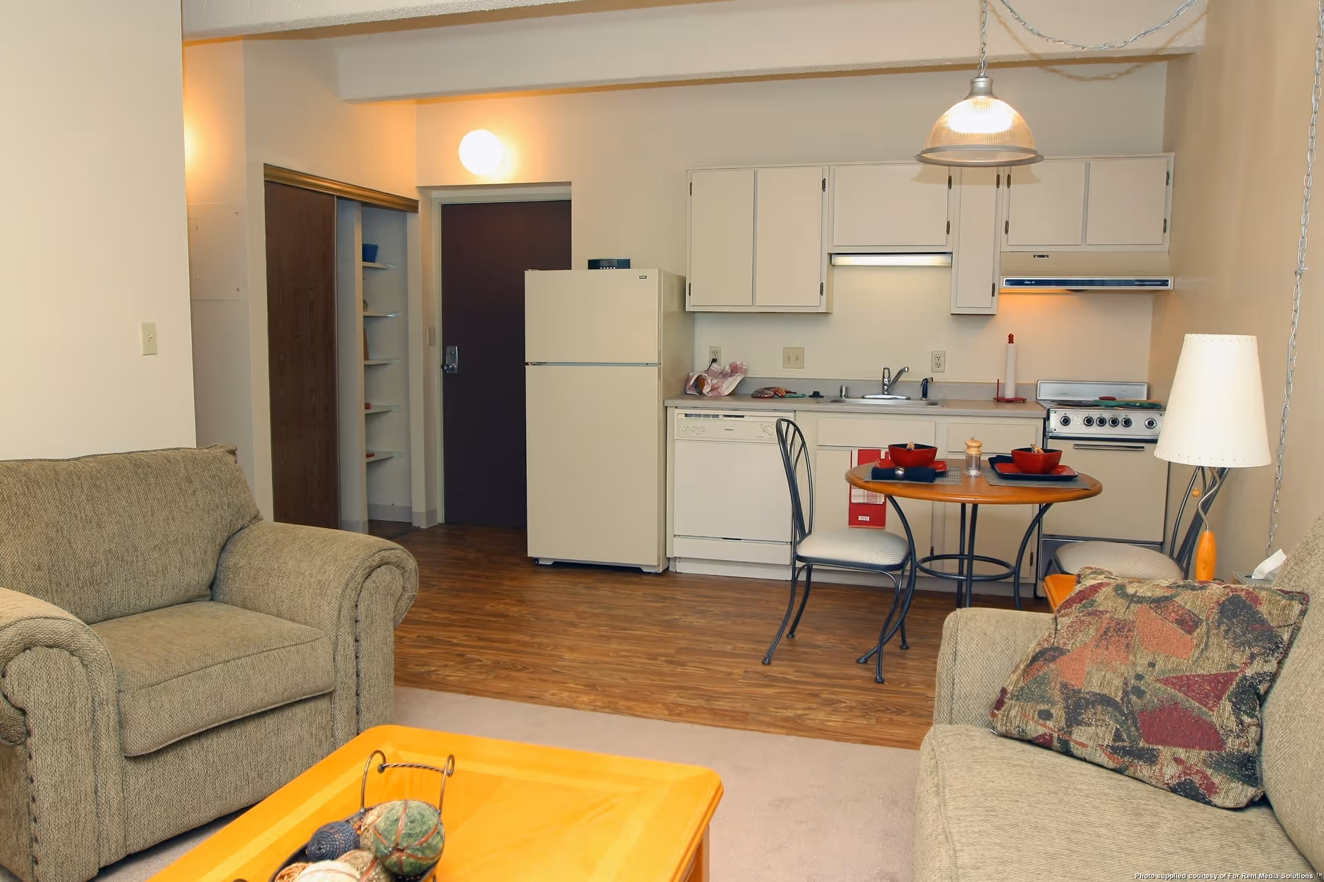 Open living room with two upholstered sofas, a coffee table, and a small kitchen with refrigerator and dining table.