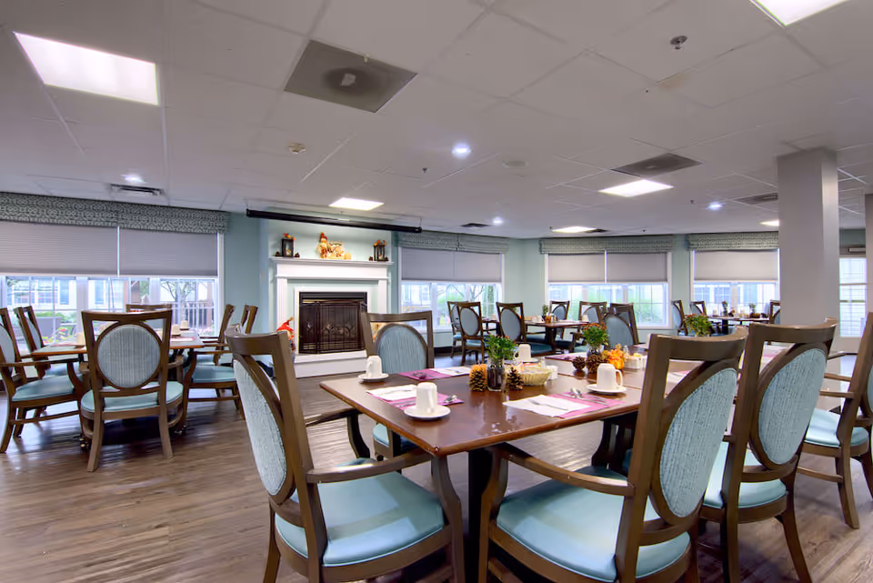 Bright communal dining room with multiple set tables and chairs and a fireplace at the far wall.