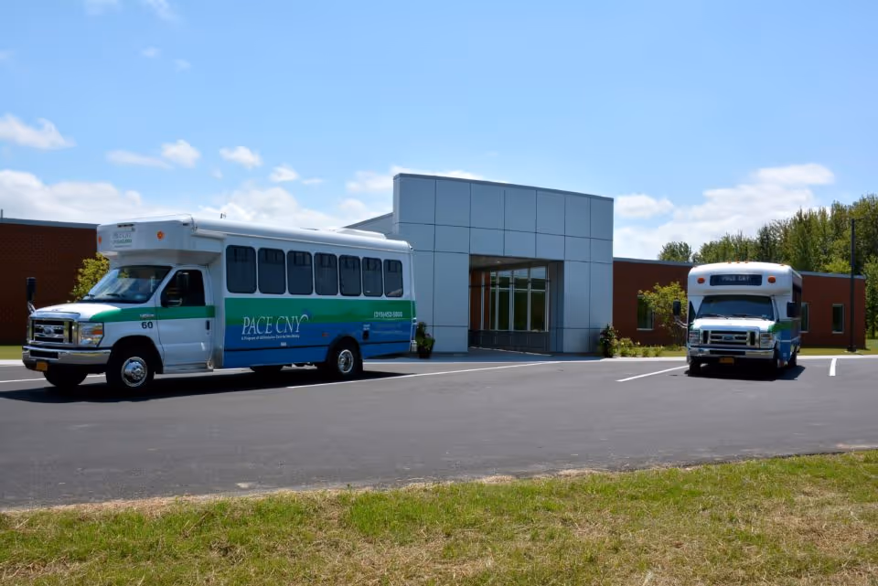Two buses parked in front of a modern building entrance at a senior living facility.