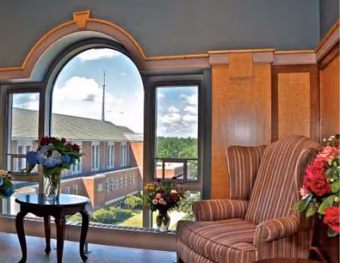 Cozy interior lounge with arched window, striped armchairs, and floral arrangements.