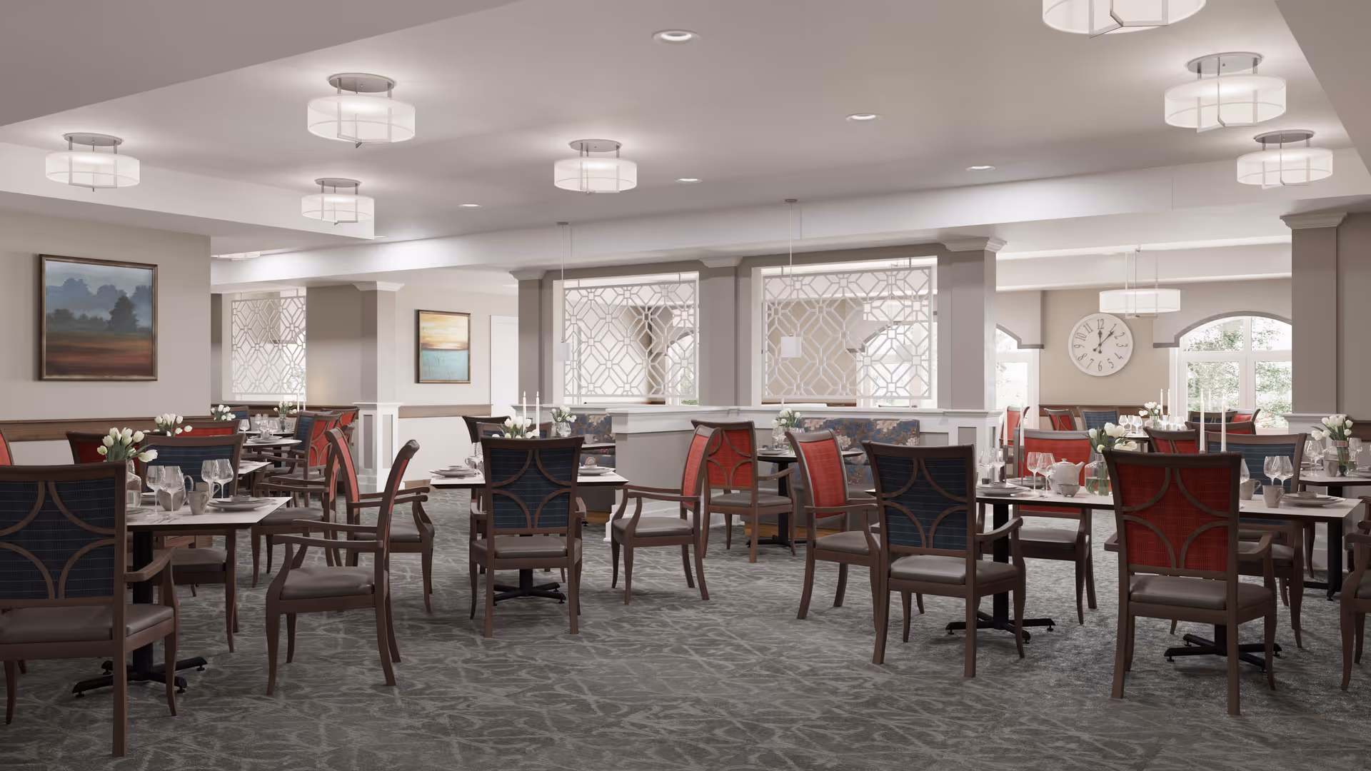 A spacious and well-lit dining room in a senior living facility with multiple tables and chairs arranged neatly. The chairs have red and dark blue upholstery, and the tables are set with glassware, plates, and small floral centerpieces. The room features soft lighting from ceiling fixtures, decorative wall art, and large windows allowing natural light to enter.