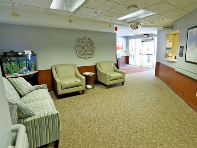 A reception hallway with a striped sofa, two armchairs, a small table, an aquarium, and double glass entrance doors.