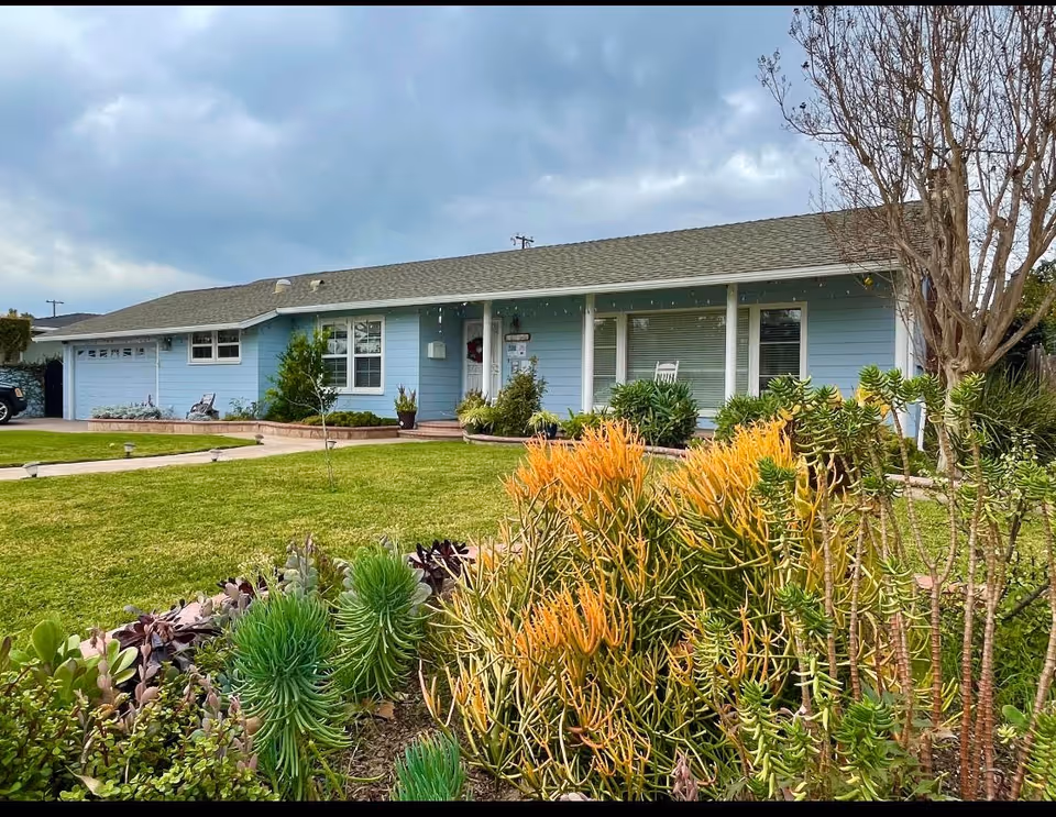 Blue single-story senior living building with a green lawn and shrubs in front.