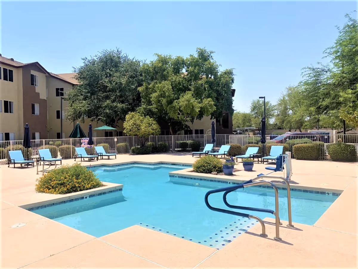 Outdoor swimming pool with lounge chairs, umbrellas, and apartment buildings in the background.