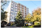 Exterior view of a multi-story residential building surrounded by trees and parked cars under a clear blue sky.