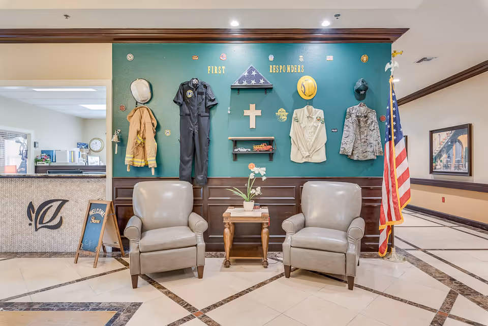 Lobby seating area with two armchairs in front of a display wall honoring first responders with uniforms, a cross, and an American flag.