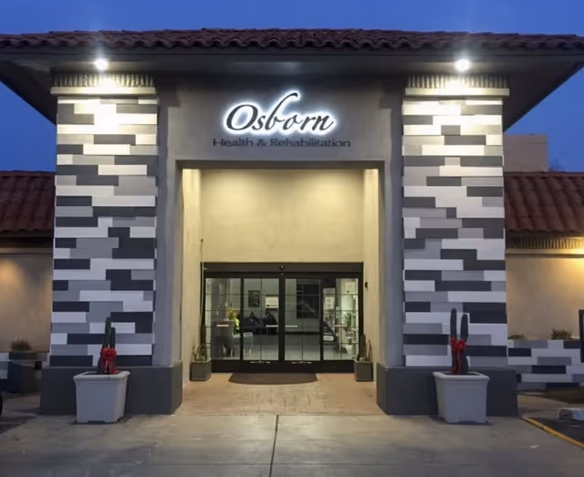 Entrance to Osborn Health & Rehabilitation with an illuminated sign above glass automatic doors flanked by patterned pillars and planters.