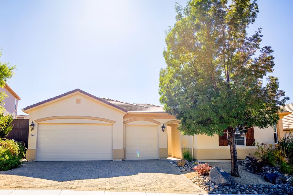Single-story facility front exterior with garage doors, driveway, and a large tree.
