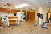 Large multipurpose common room with a kitchenette, dining tables, and exercise equipment.