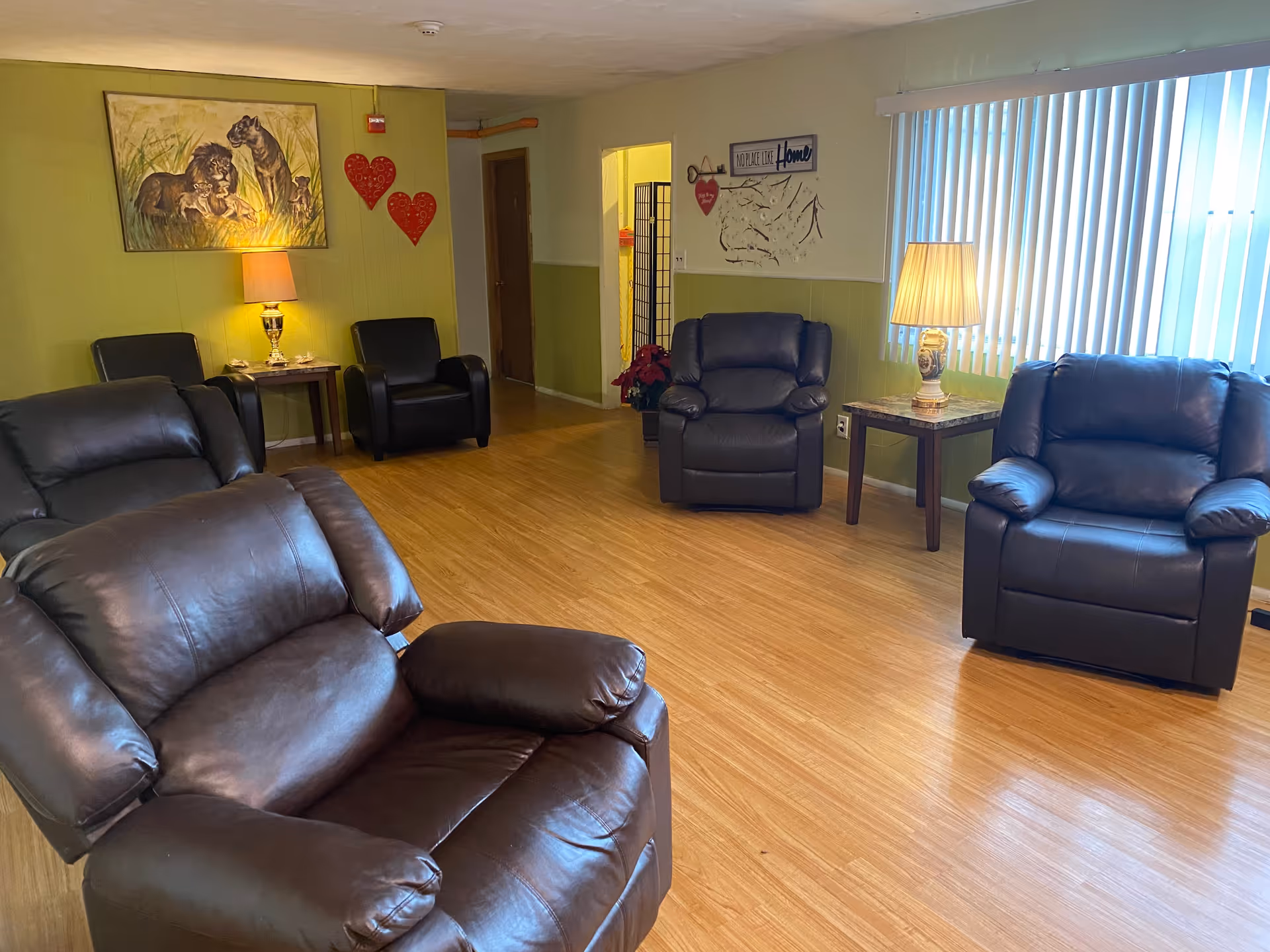 Spacious senior living lounge with leather recliners, side tables, lamps, and wall art.