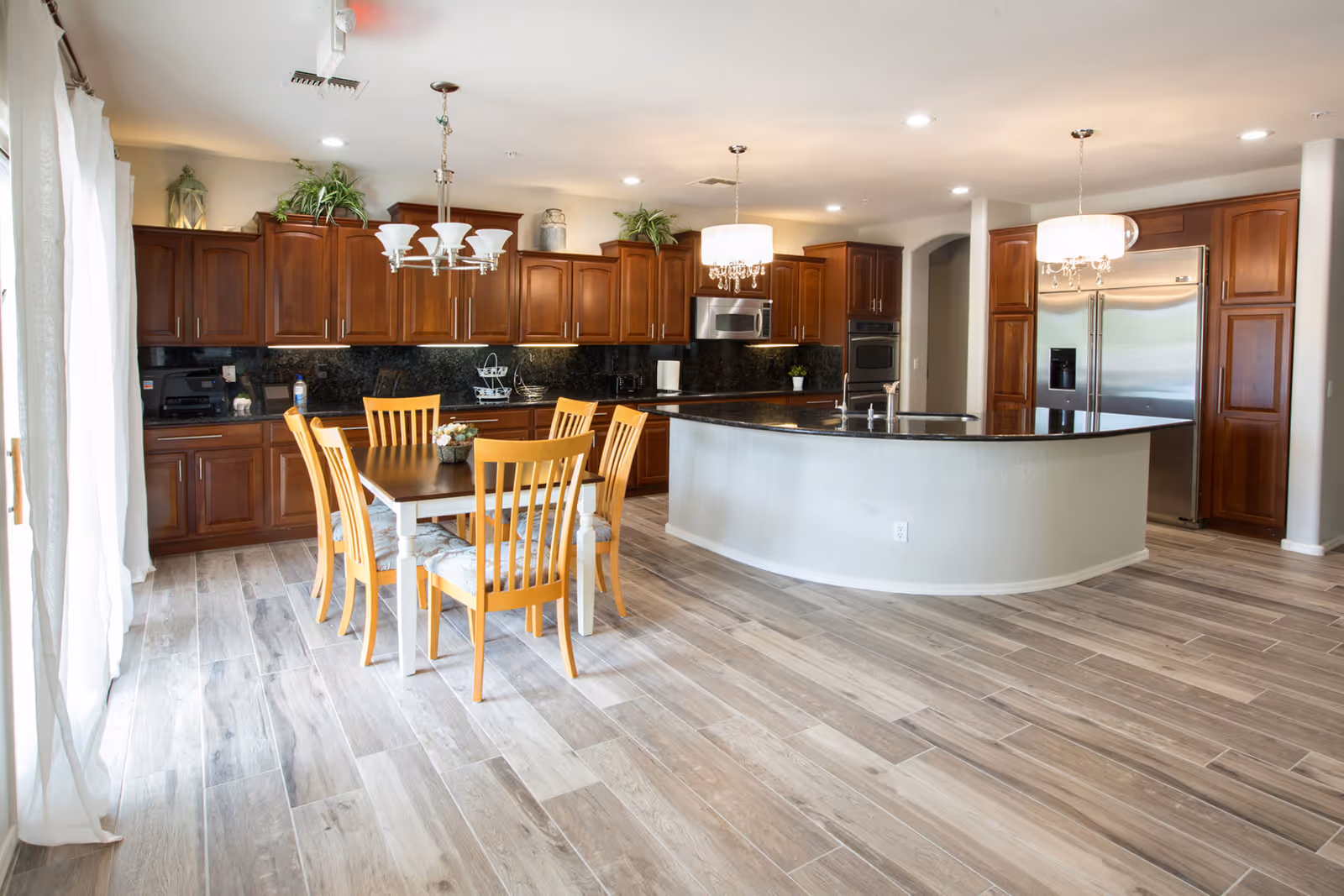 Spacious open kitchen with a large curved island, wooden cabinets, stainless steel appliances, and a dining table with chairs.