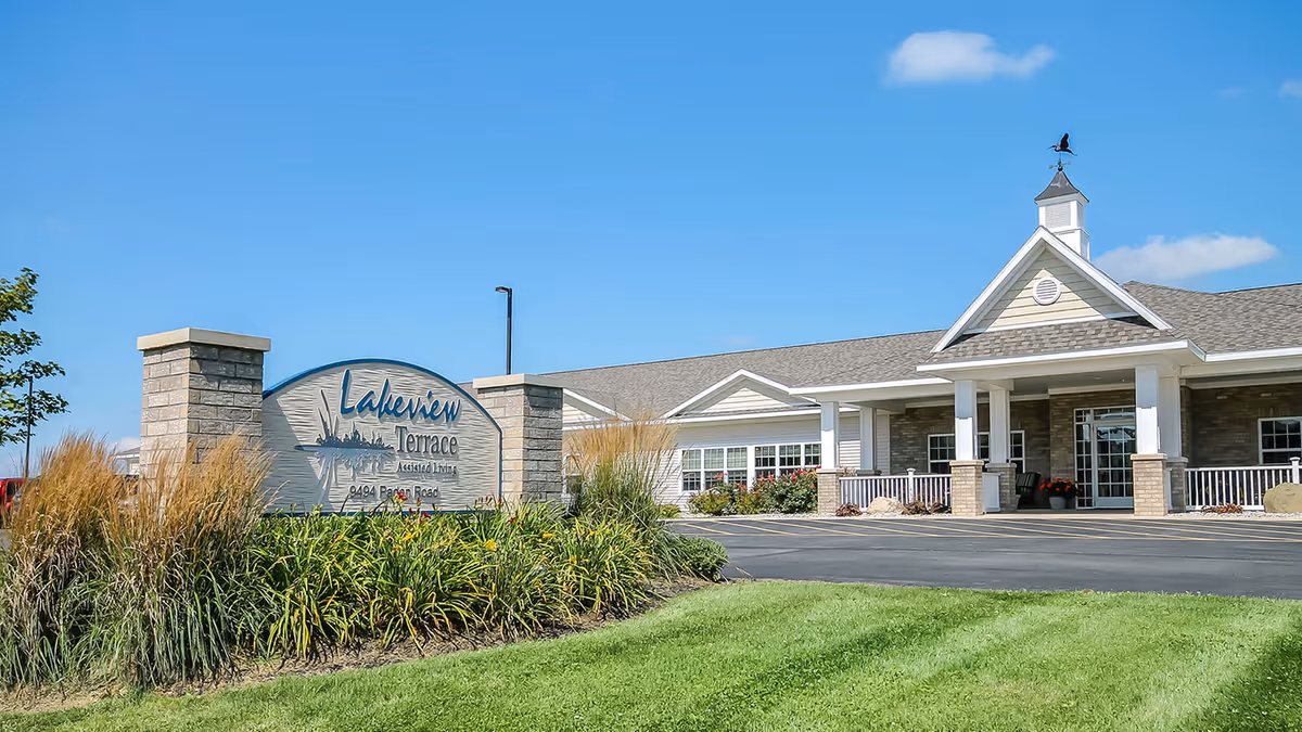 Front exterior of Lakeview Terrace Assisted Living with a landscaped sign, entrance driveway, and building facade under a clear blue sky.