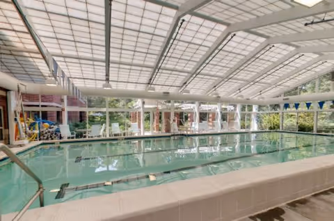 Indoor swimming pool under a glass-paneled ceiling with lane markers and seating along the windows.