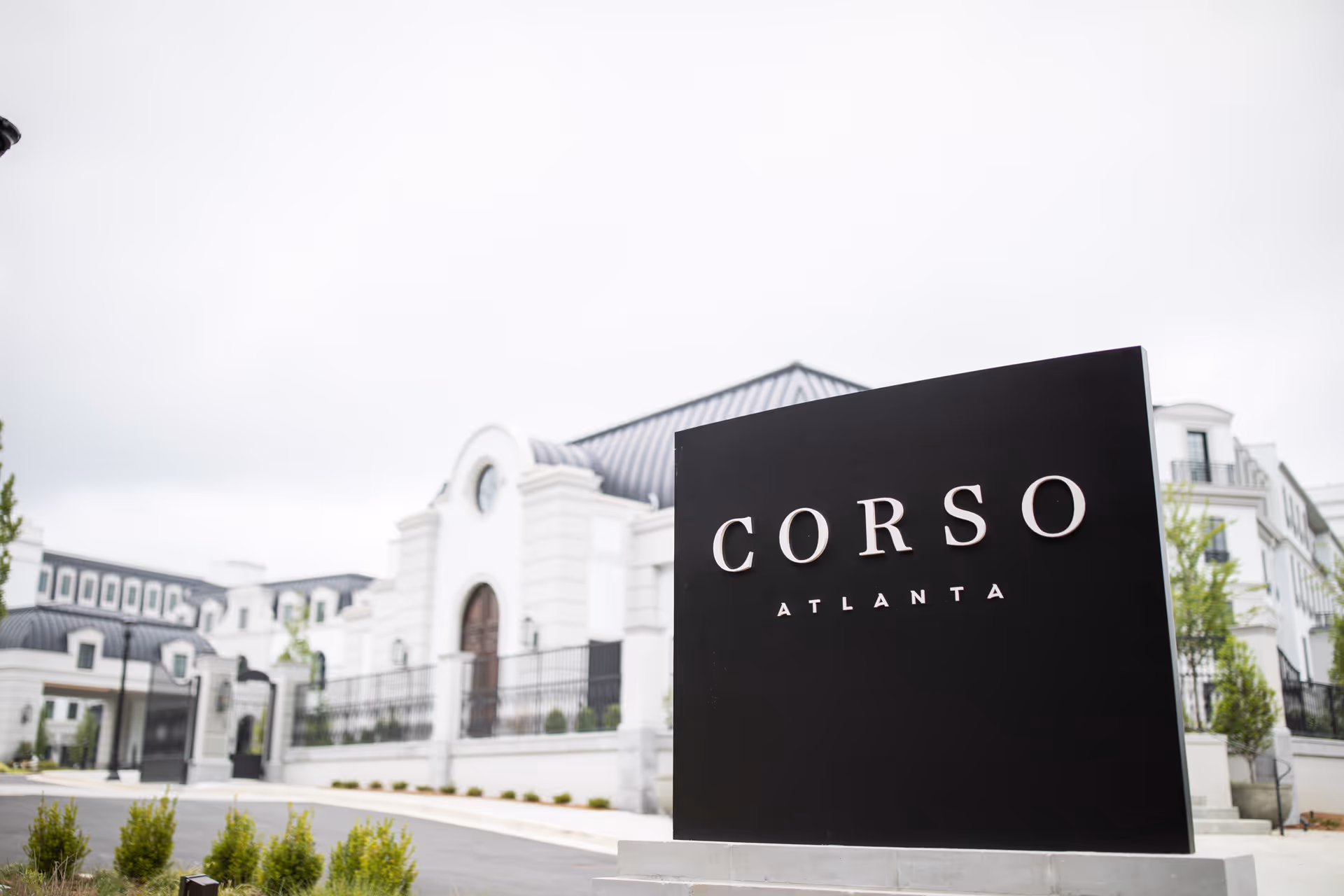 Black entrance sign reading 'CORSO ATLANTA' in front of a large white multi-story building with a dark roof.