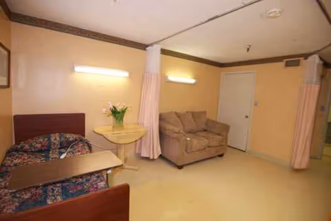 A small senior living bedroom with a bed, sofa, side table, and curtains.