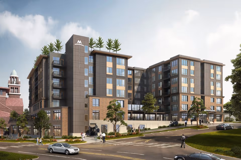 Exterior view of a modern multi-story senior living facility named Merrill Gardens at Wright Park, featuring large windows, balconies, and landscaped surroundings with trees and a few people walking nearby. The building has a mix of brick and dark paneling with a clear sky in the background.