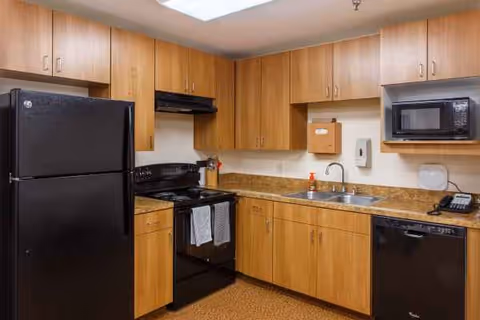Compact kitchen with wooden cabinets, fridge, stove, sink, and microwave.