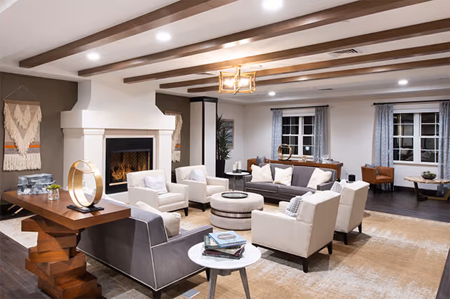 Spacious communal living room with sofas and armchairs arranged around a fireplace under exposed wooden ceiling beams.