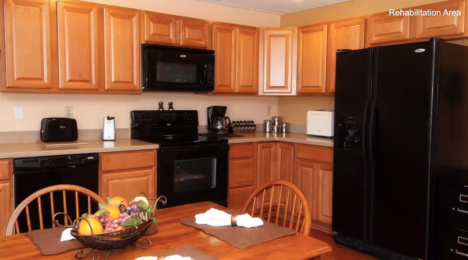 A kitchen with wooden cabinets, black appliances, and a dining table with a fruit centerpiece.