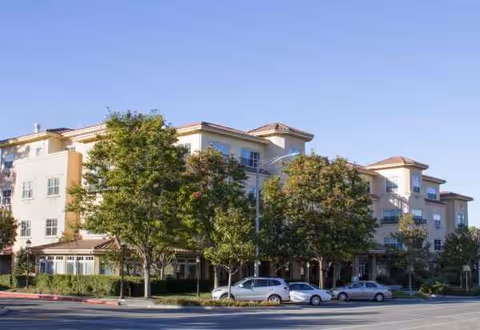 Sunrise of Sunnyvale senior living building exterior with trees and parked cars along the street.